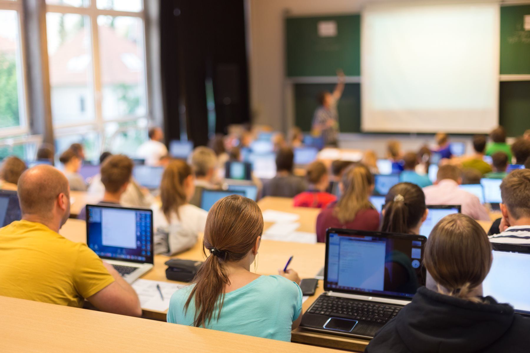 A group of people are sitting in a lecture hall with laptops.