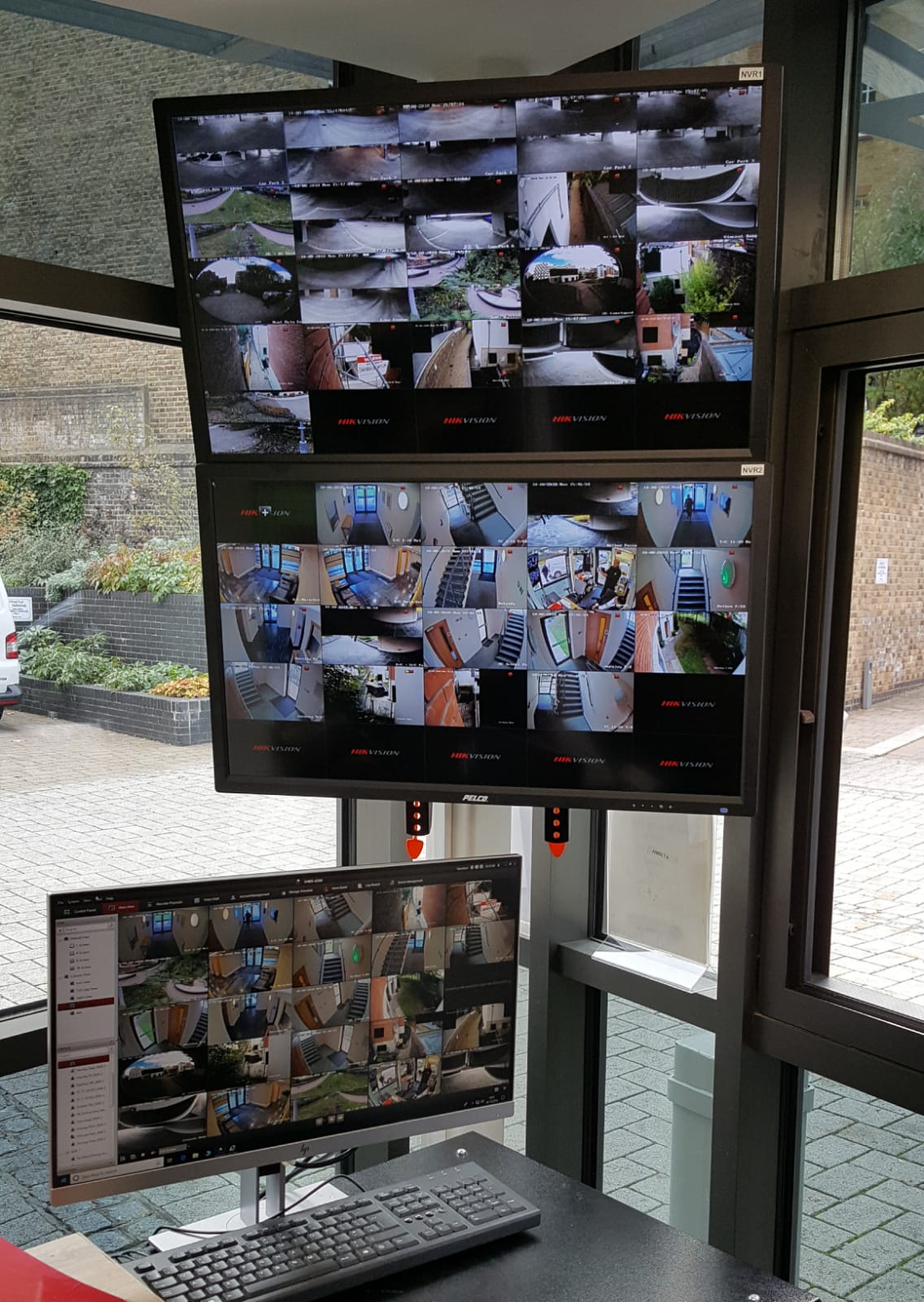 Two monitors are sitting on a desk in front of a window.