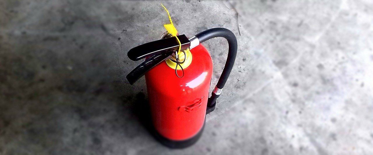 A red fire extinguisher is sitting on a concrete floor.