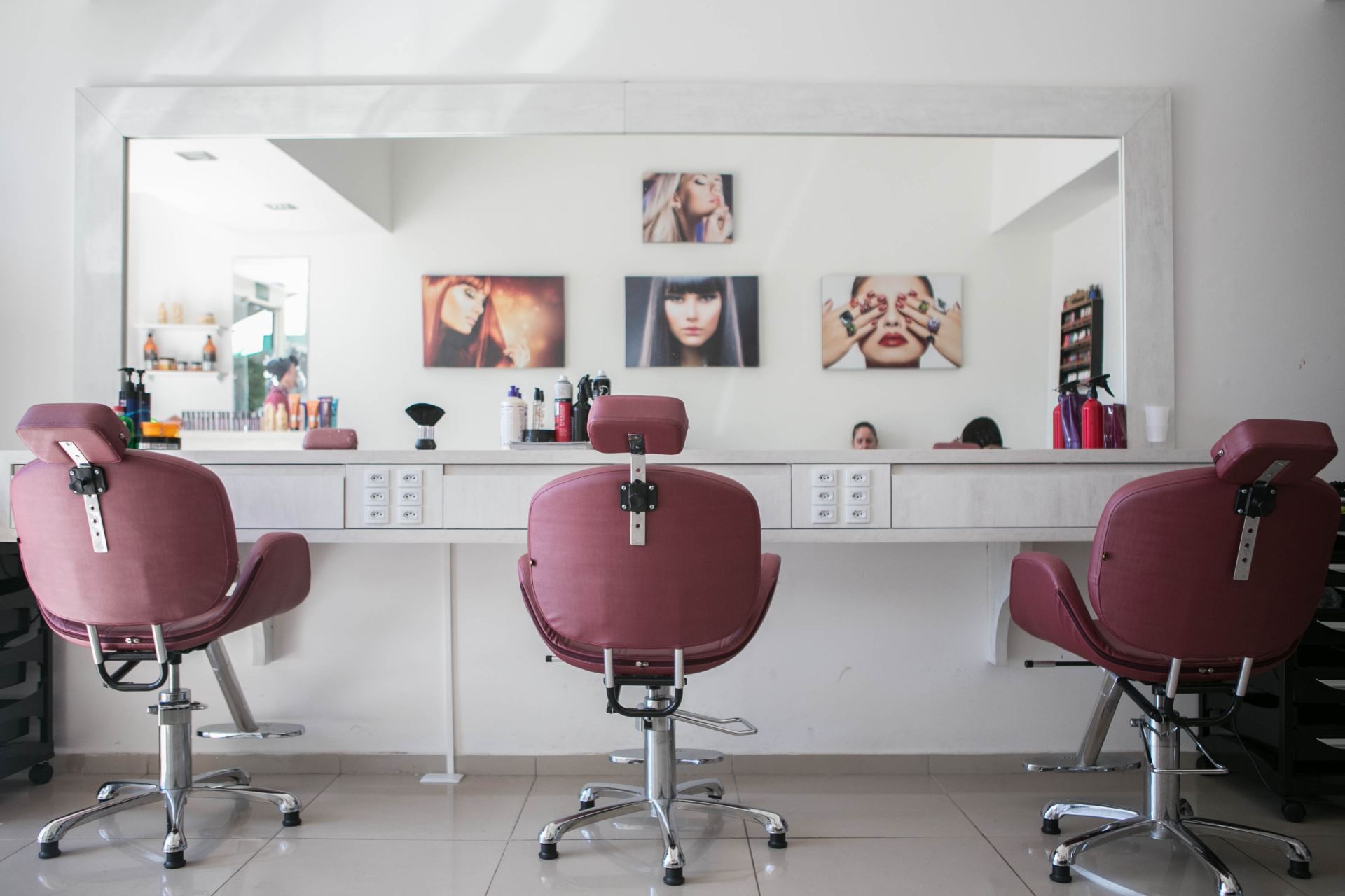 There are three chairs in a hair salon with a large mirror.