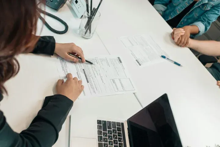 A woman sitting at at a desk across from two people with paperwork on top.
