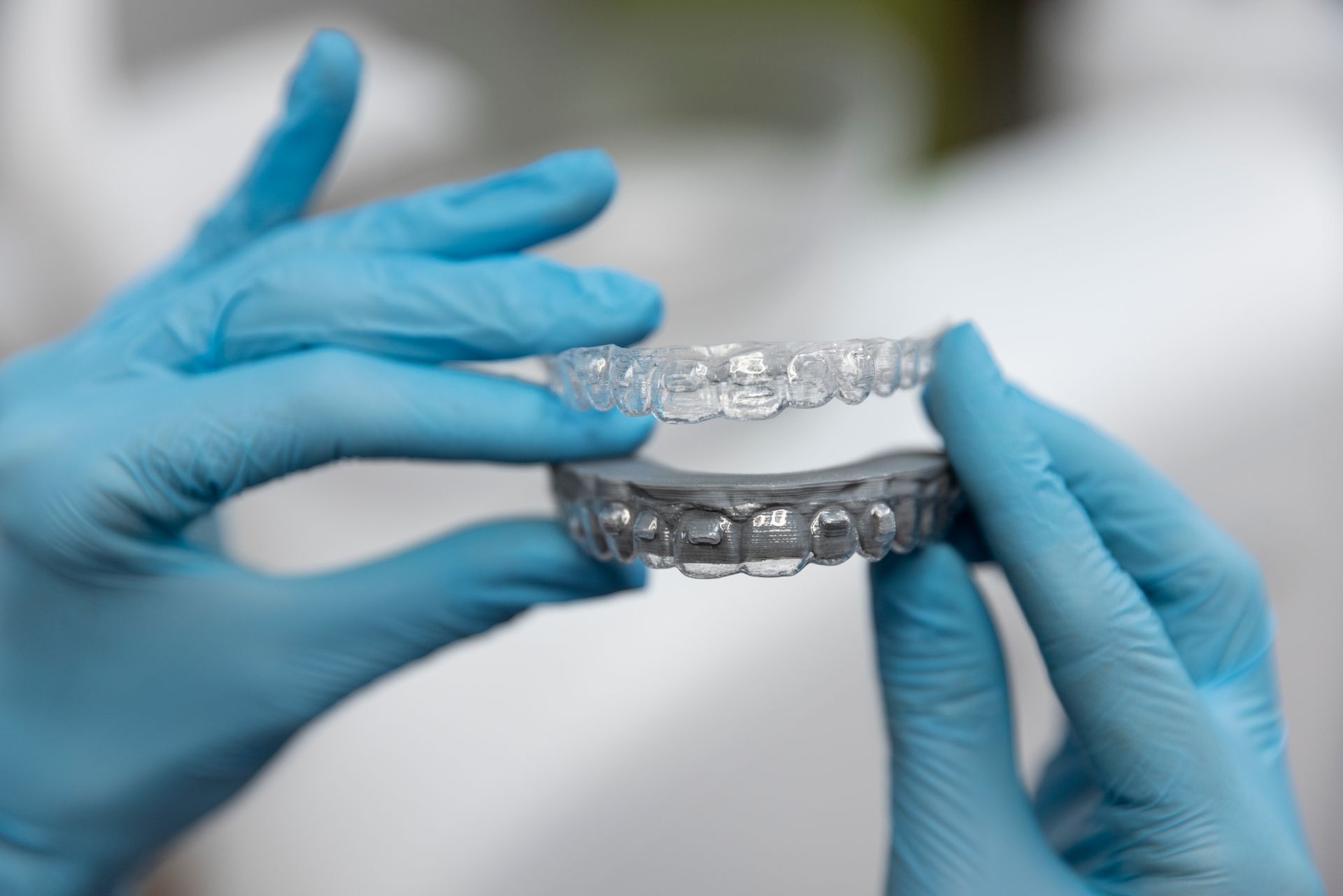 A person wearing blue gloves is holding a clear retainer in their hands.