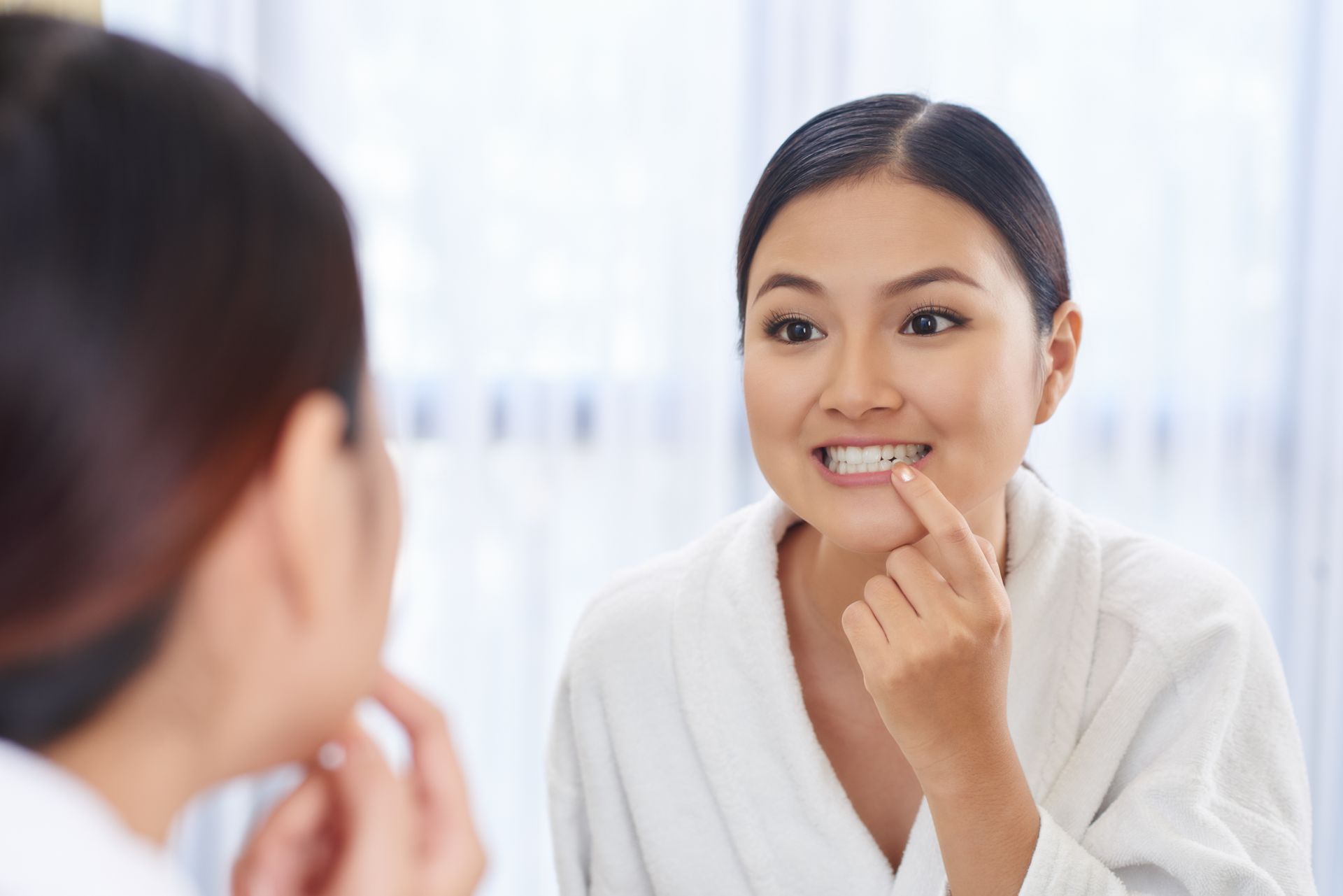 A woman is looking at her teeth in the mirror.