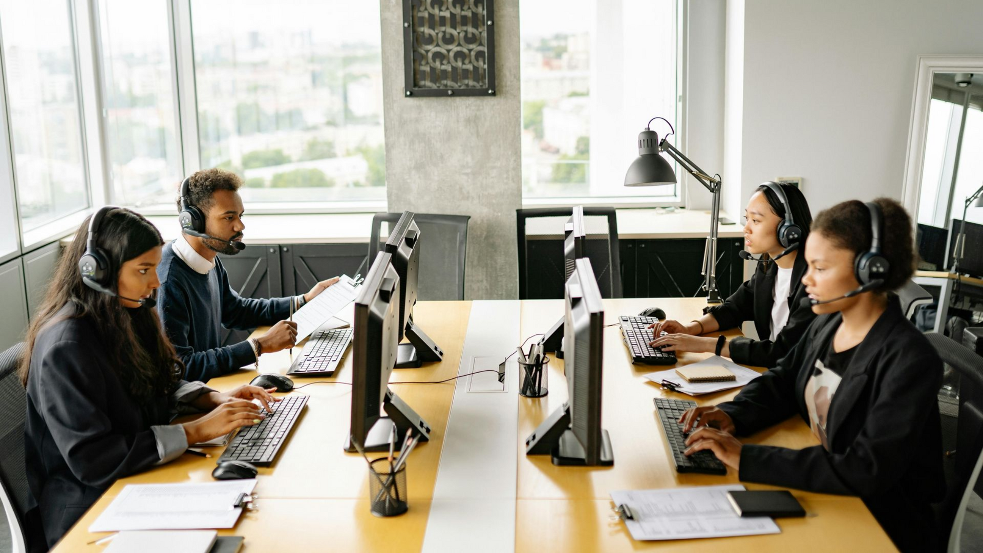 People working at computers with headsets in a modern office setting.