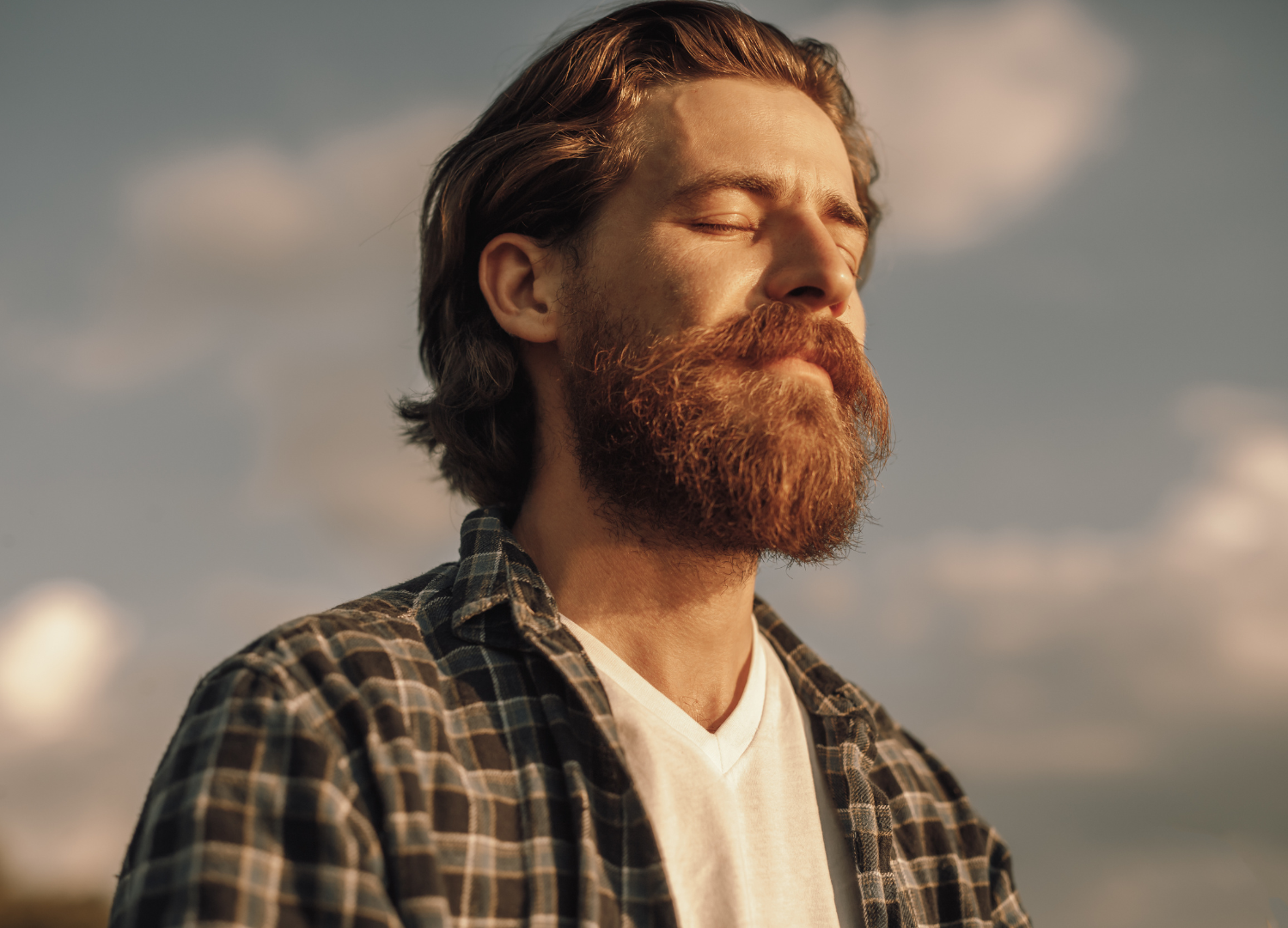 A man with a beard and long hair is standing with his eyes closed.