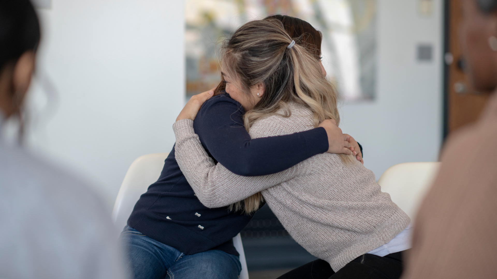Two women are hugging each other in a group therapy session.