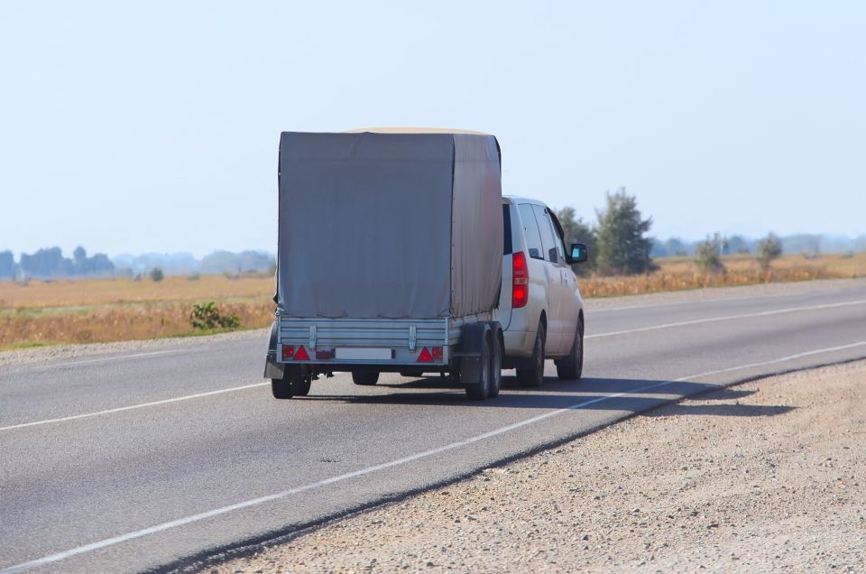A white truck is towing a trailer on a highway.