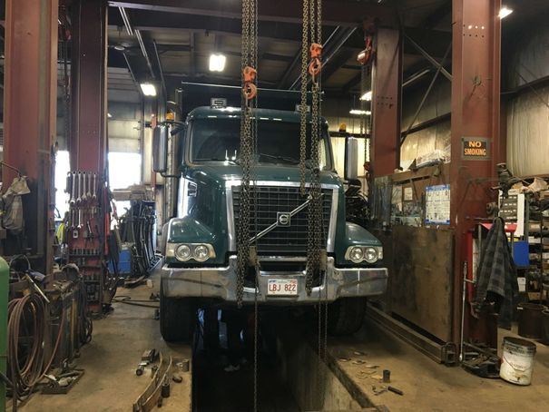 A dump truck is being lifted by a crane in a garage.