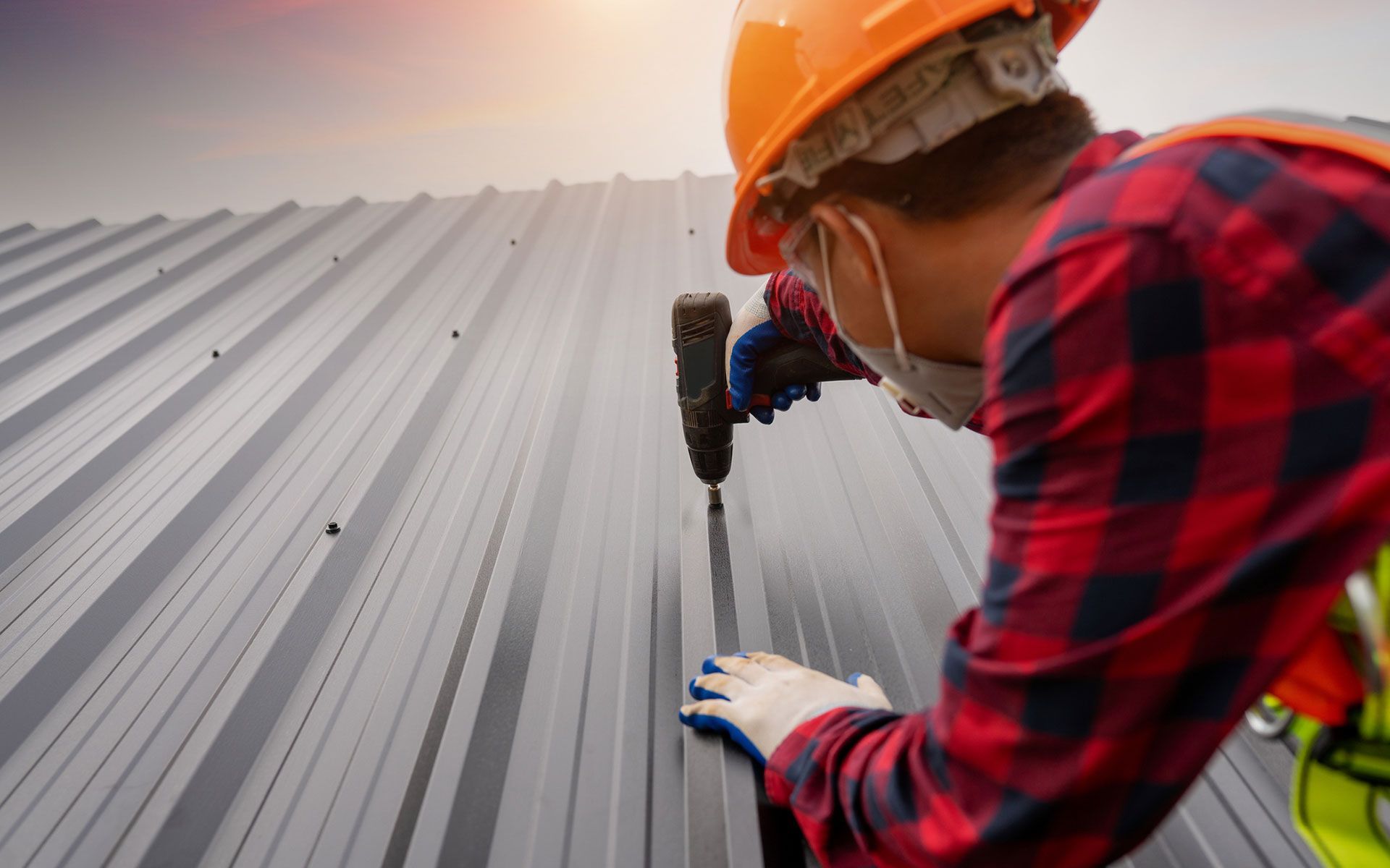 A man is working on a metal roof with a drill.