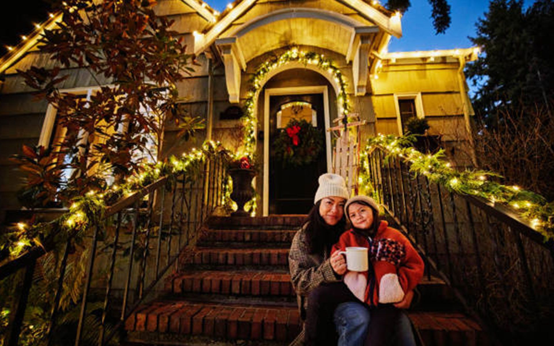 A woman and a child are sitting on the steps of a house decorated for christmas.