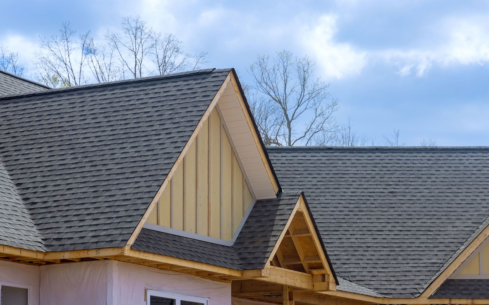 A house under construction with a gray roof and a blue sky in the background.