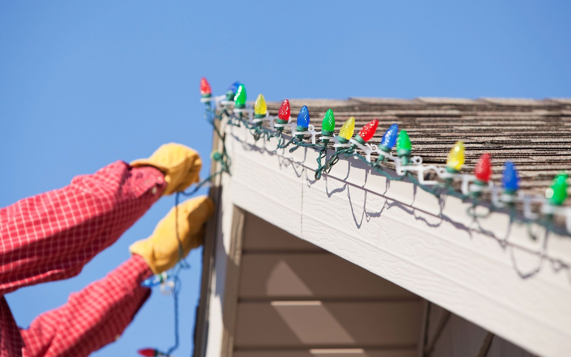 A person is hanging christmas lights on the side of a house.