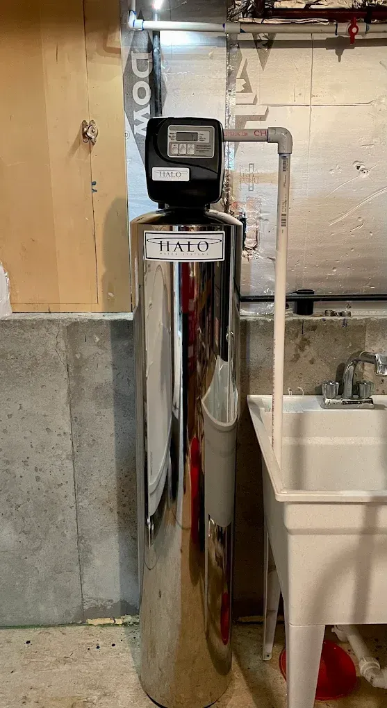 A water softener is sitting in a laundry room next to a sink.