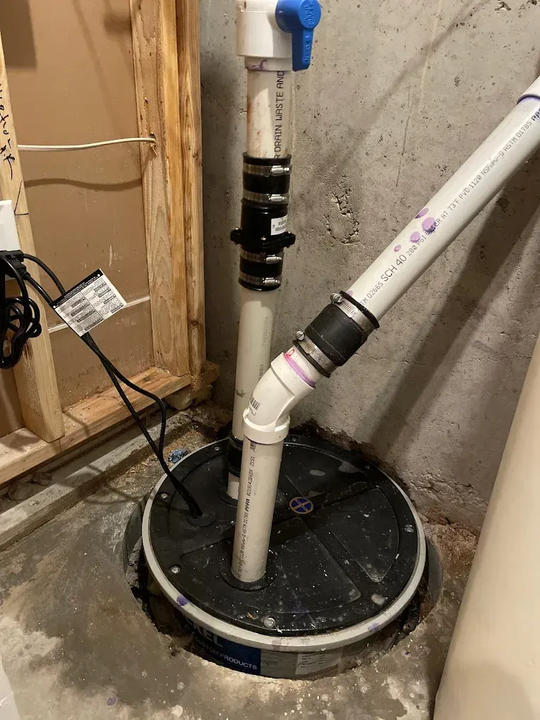 A sump pump is sitting in a basement next to a water heater.