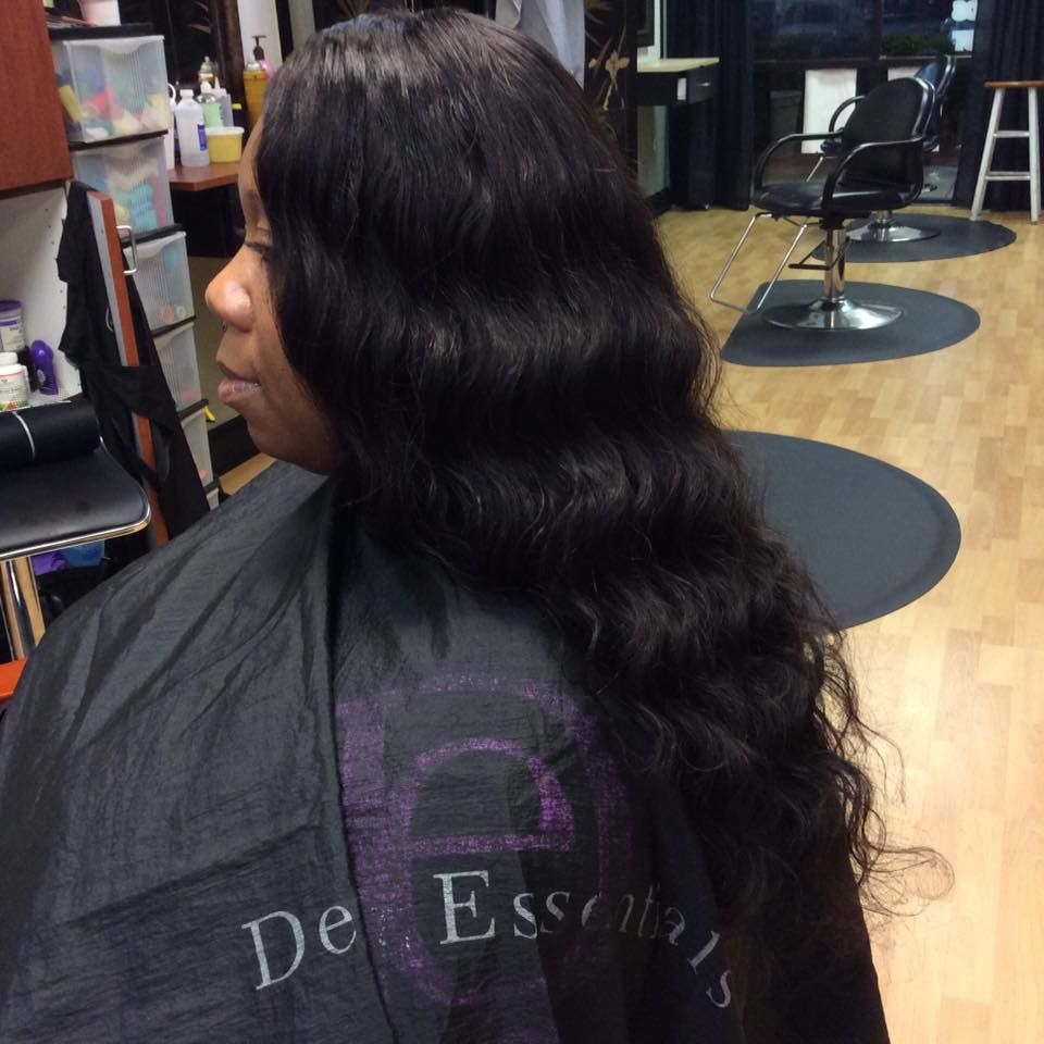 Woman in a salon with long, wavy black hair. She is wearing a black cape.