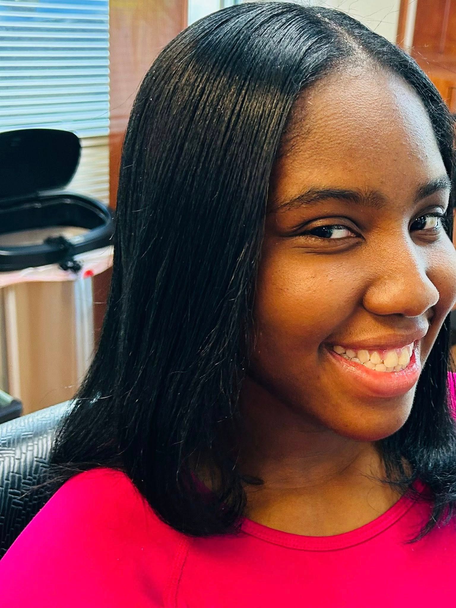 Smiling Black woman with straight, dark braided hair; wearing a pink top.