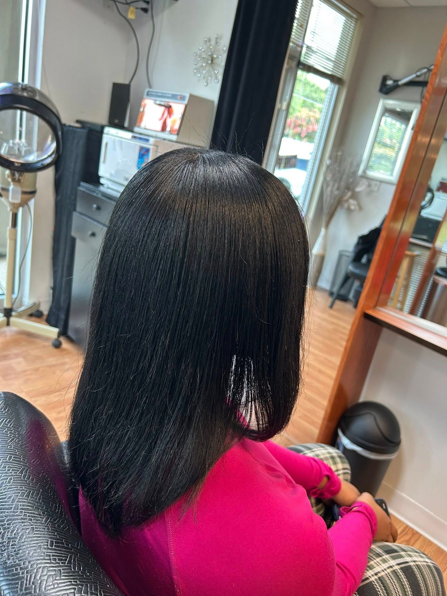 Person with sleek, straightened black hair in a pink top at a hair salon.