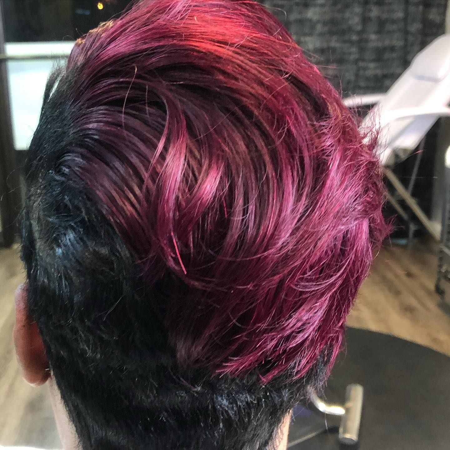 A person with a short hairstyle, black roots transitioning to vibrant red-purple hair.