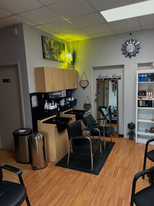 Hair salon interior: shampoo station, chairs, products on shelves, mirror, and a clock on the wall.