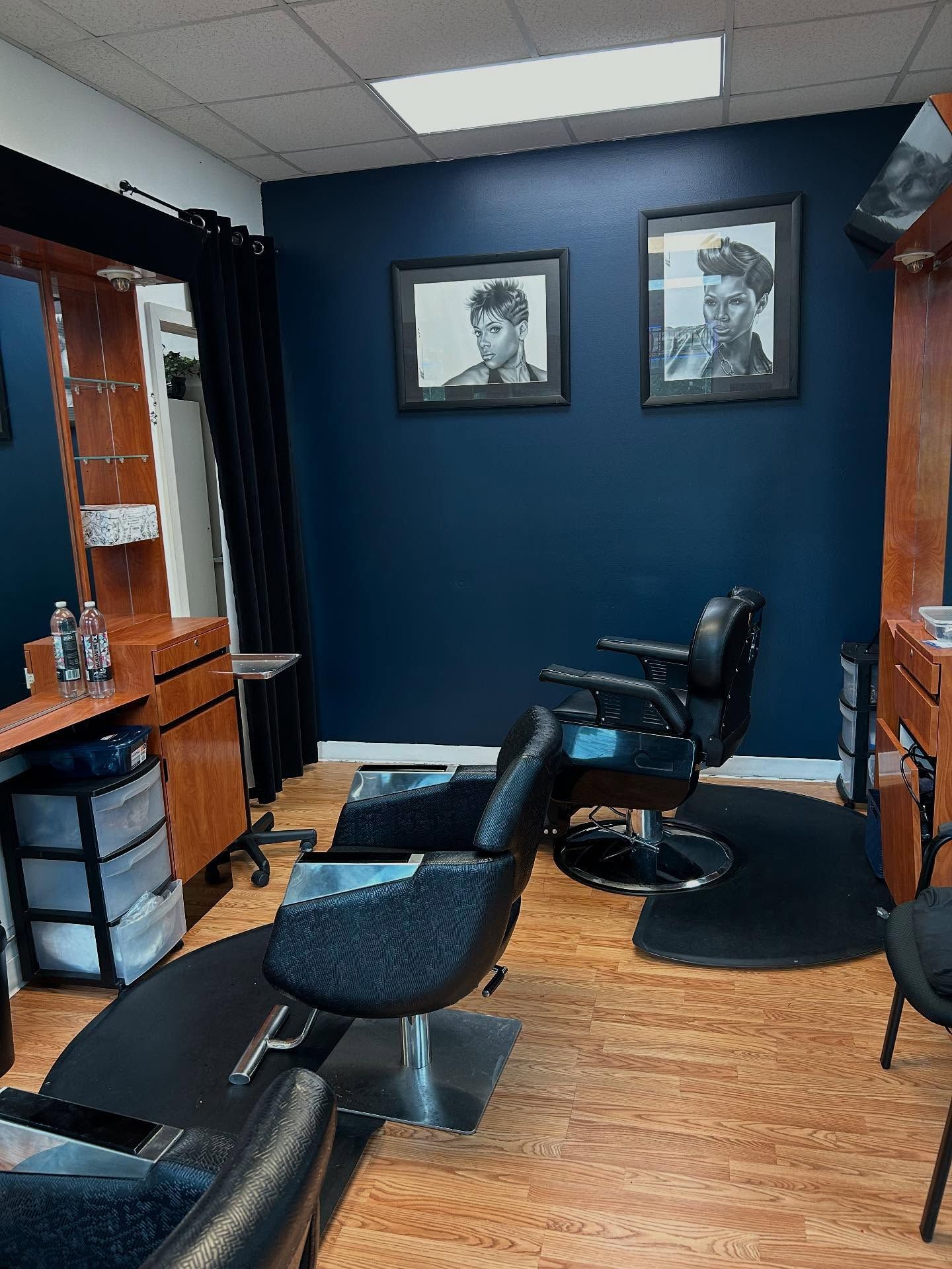 A barber shop interior with dark blue walls, black chairs, Elvis portraits, and wooden cabinets.