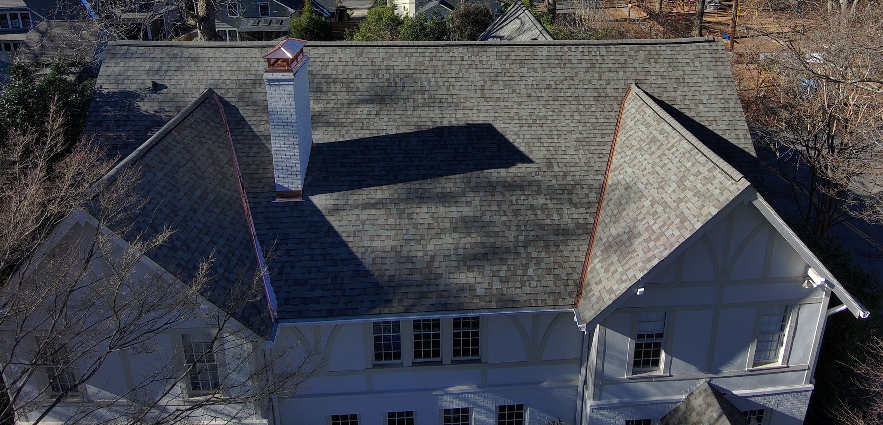 A two-story white Tudor-style house with new roof, copper valleys, and copper chimney caps.