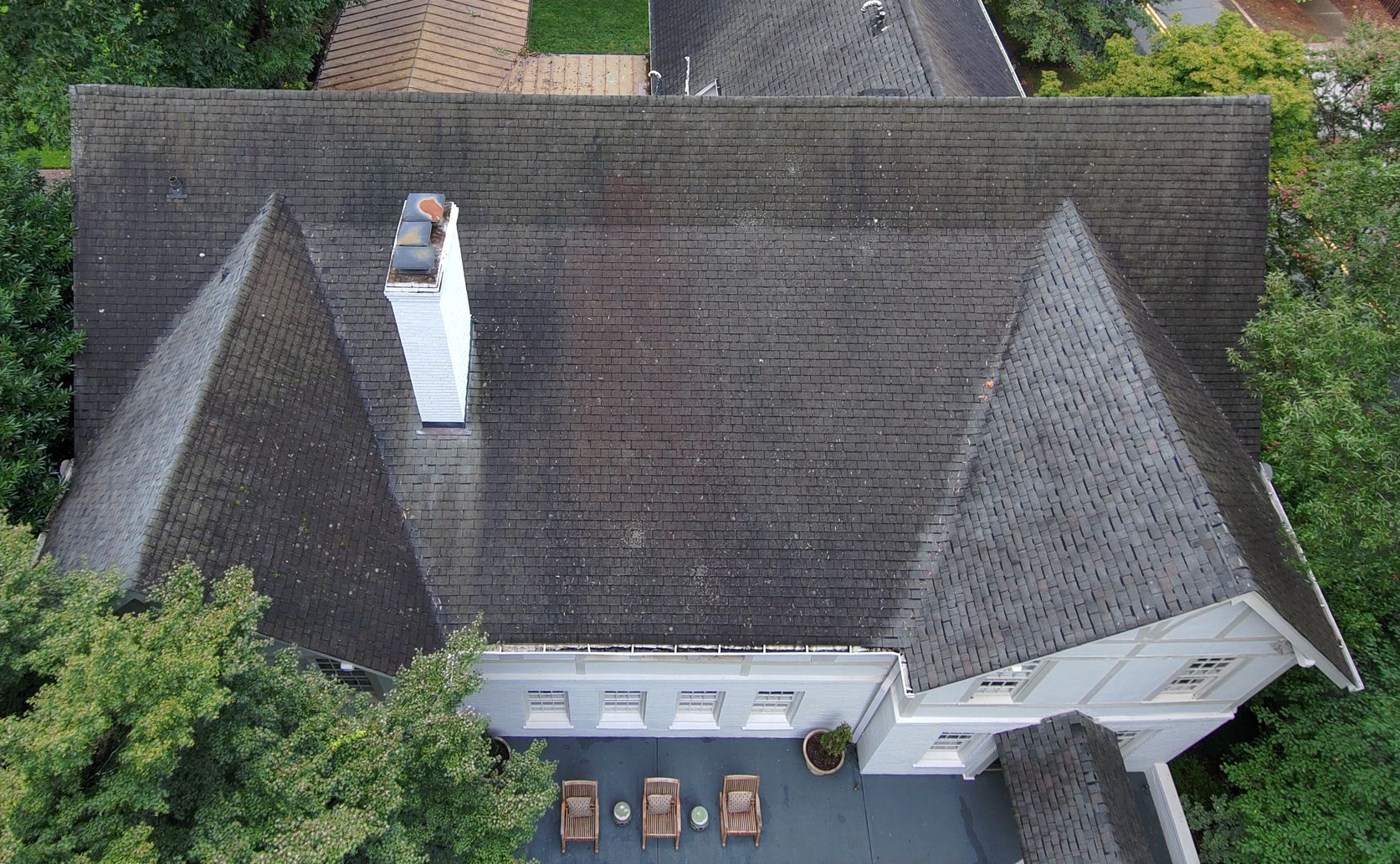 A two-story, white Tudor-style house with timber detailing, a chimney, and a small front porch, surrounded by shrubbery.