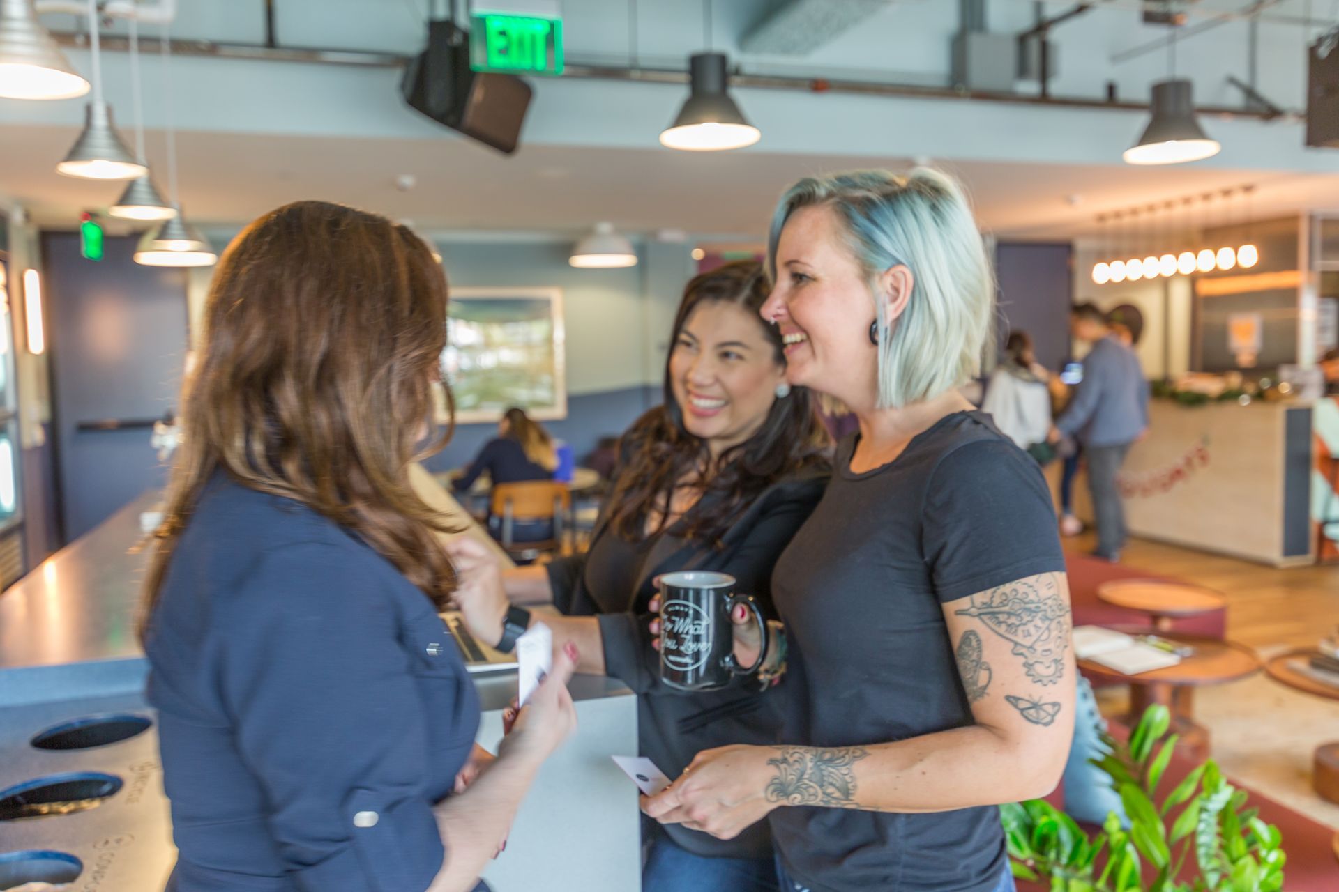 Three women are standing next to each other in a room talking to each other.