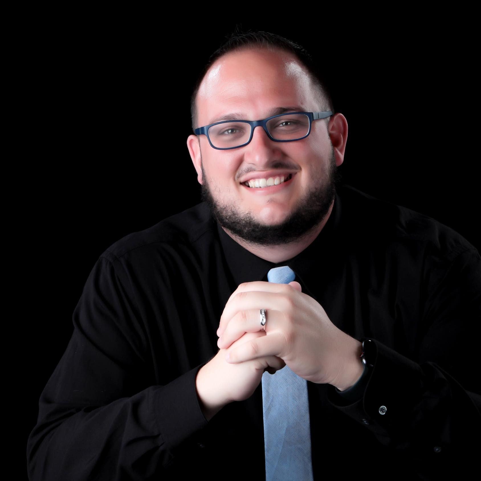 A man wearing glasses and a tie is smiling for the camera
