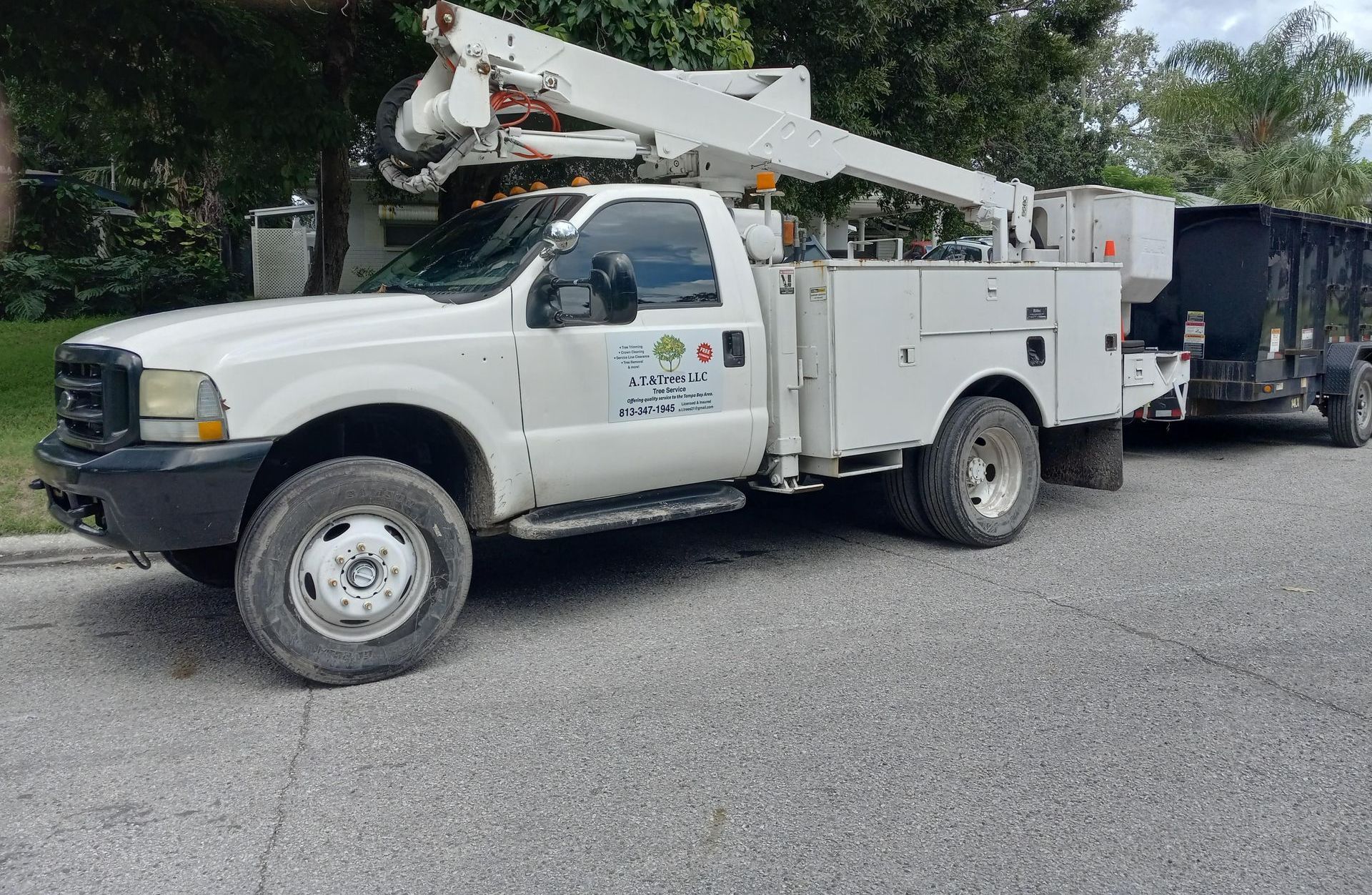 A white truck with a crane on top of it is parked on the side of the road.
