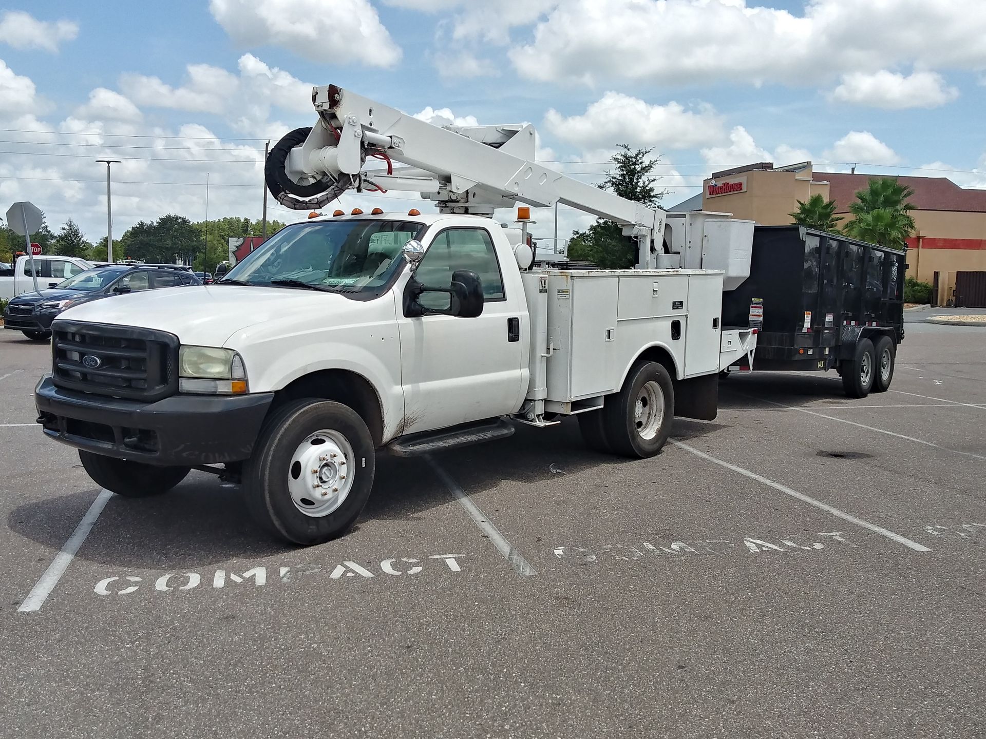 A white truck with a crane on top of it is parked in a parking lot.