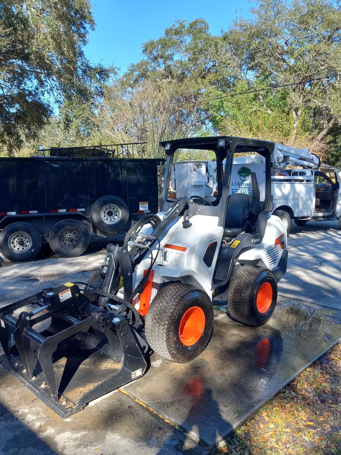 A small tractor with a grapple attached to it is parked on the side of the road.