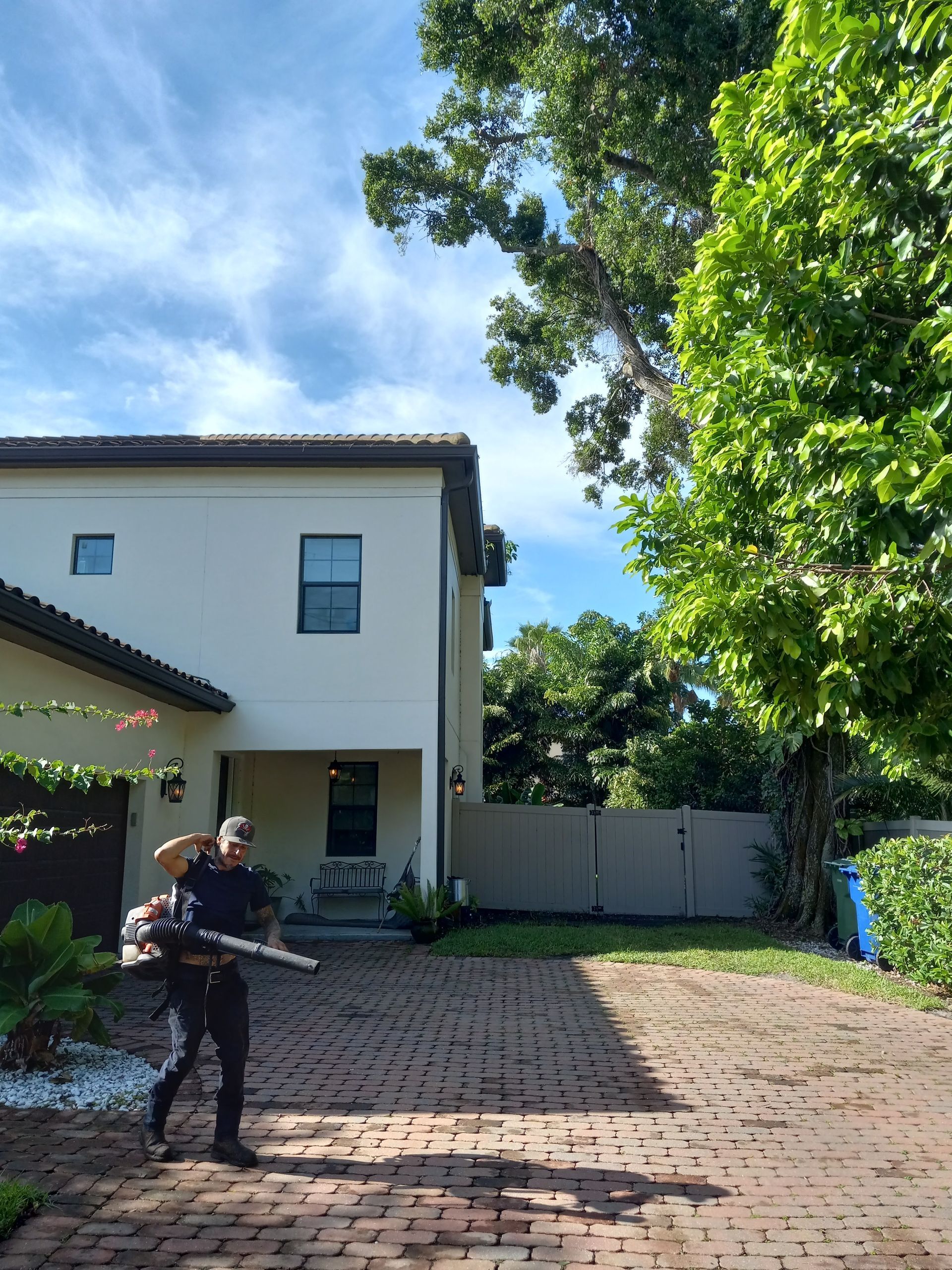 A man is spraying a brick driveway in front of a house.