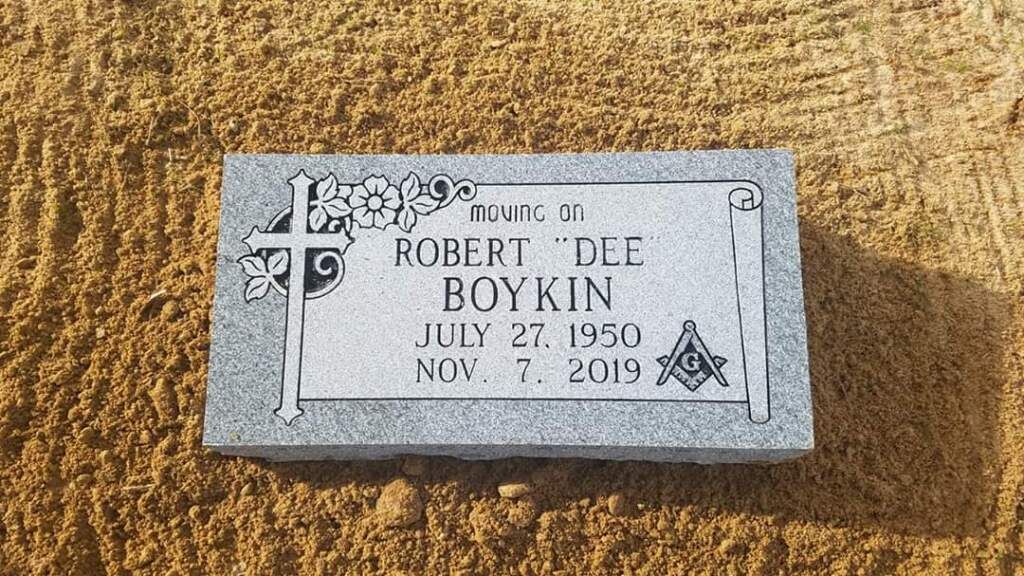 a gravestone for robert def boykin is sitting in the sand .