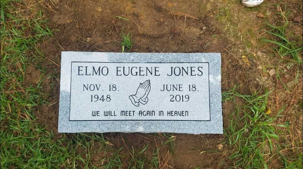 a gravestone for elmo eugene jones is sitting in the grass .