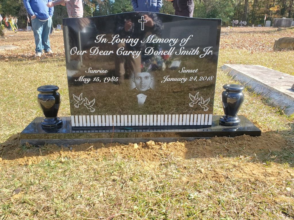 a black gravestone with a picture of a man on it in a cemetery .