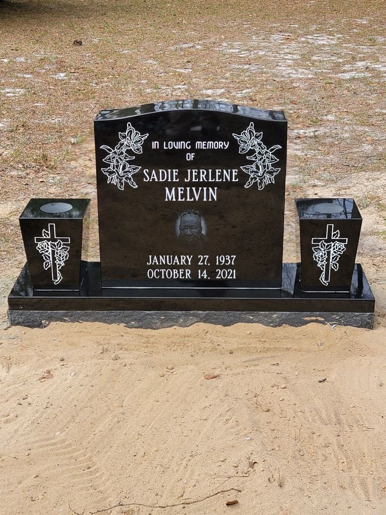 a black gravestone with two vases and a cross on it