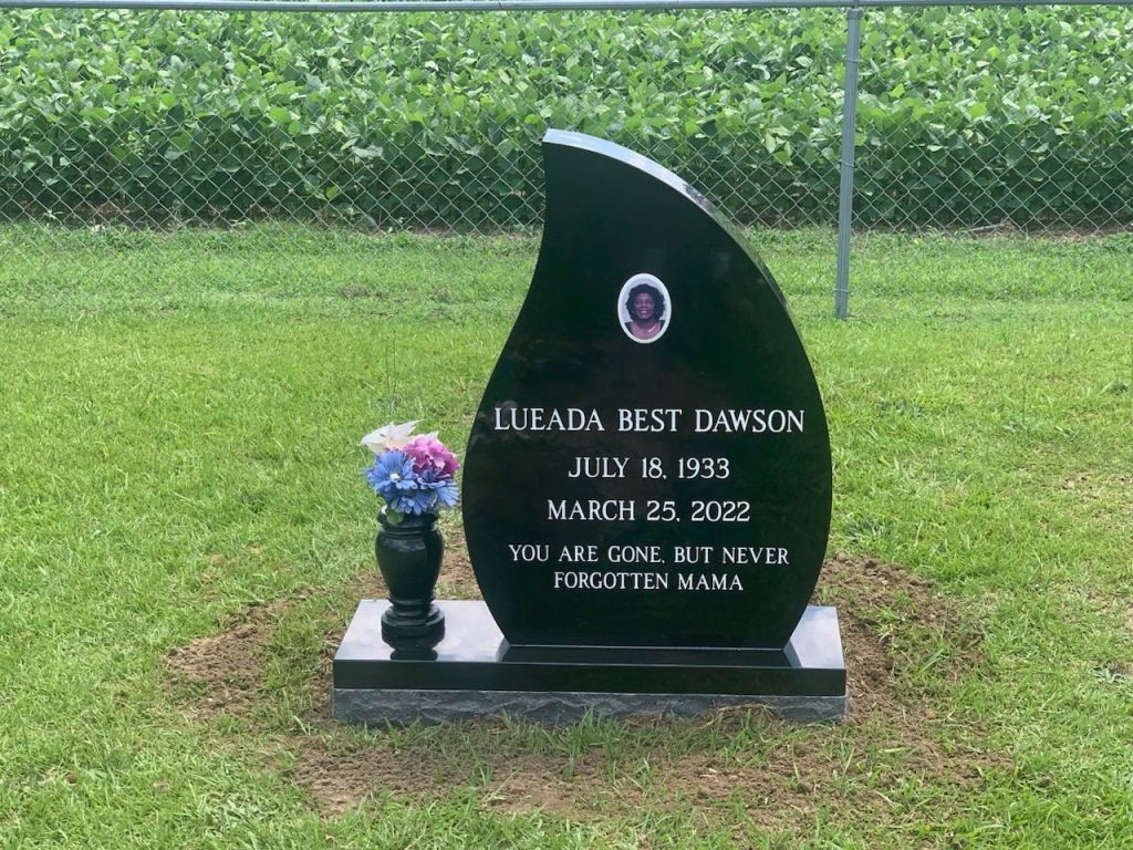 a black gravestone in the shape of a teardrop with flowers in a vase .