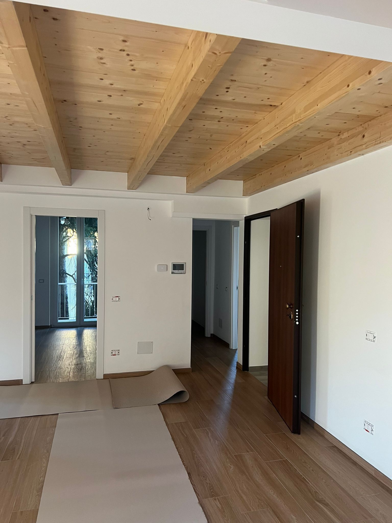 Finestra bianca, con un pannello aperto, che si affaccia su alberi verdi e su un interno dai toni gialli.