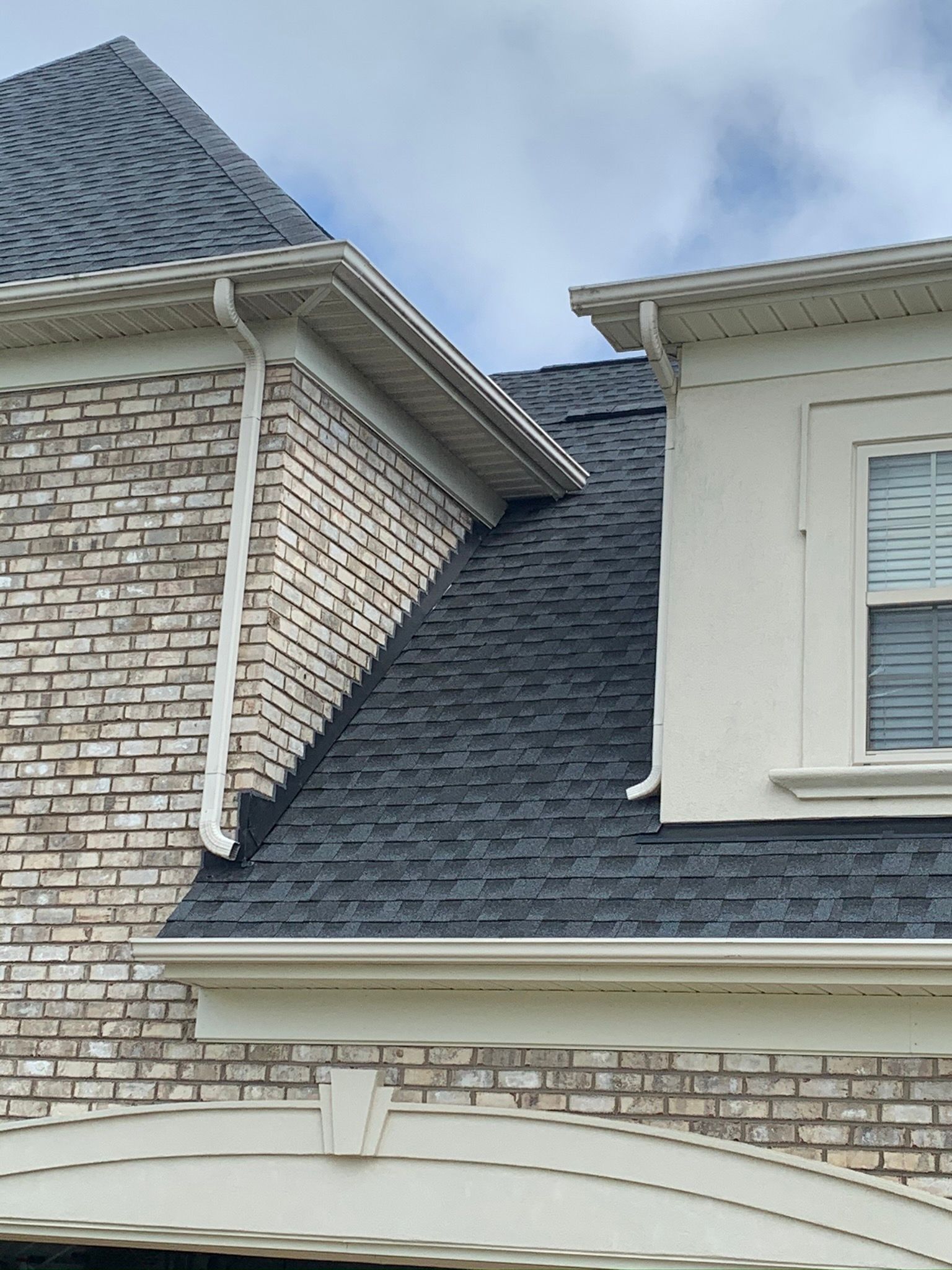 A brick house with a black roof and a window.