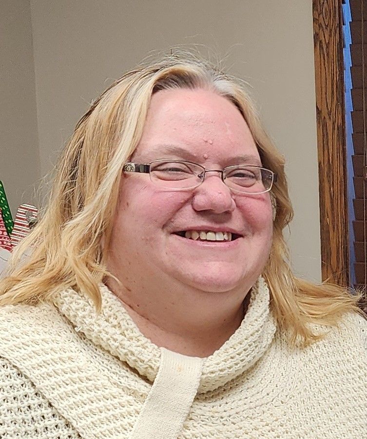 Woman wearing glasses and a cream-colored sweater smiles.
