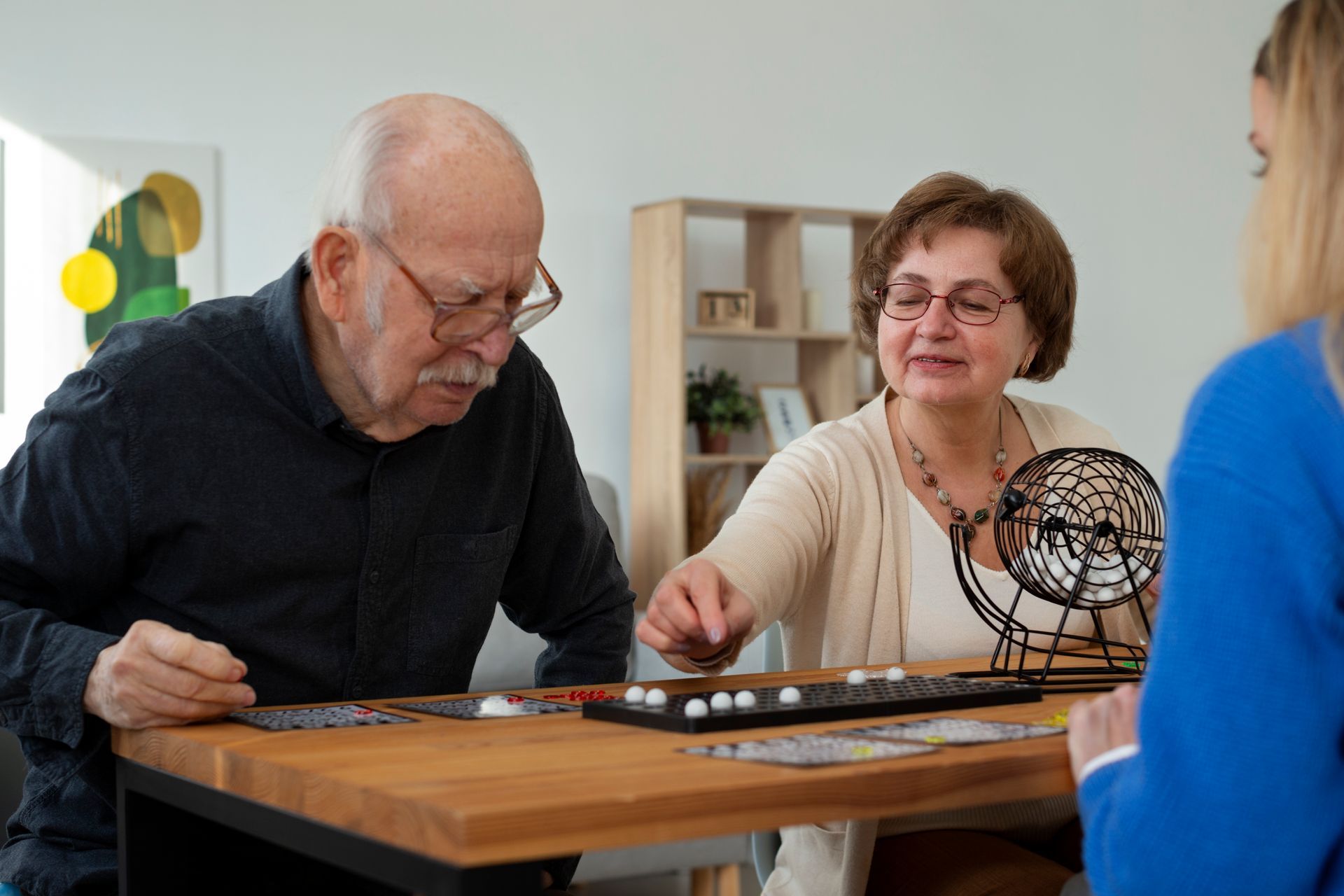 Two people playing bingo at a wooden table, one person spins the bingo cage.