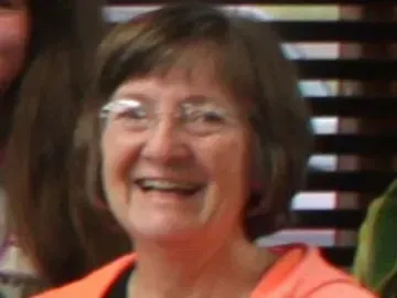 Woman with short brown hair and glasses smiling. Wearing an orange shirt.