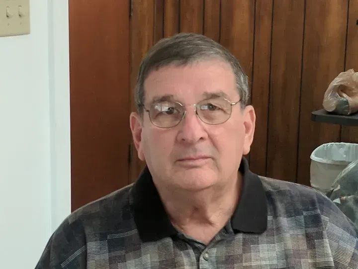 Man wearing glasses and a patterned shirt, looking directly at the camera.