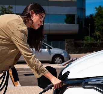 Woman plugging in electric car at charging station.