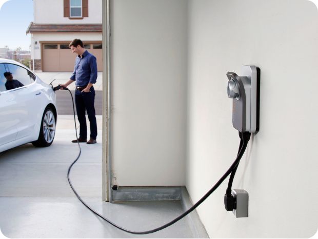 Man charging a white electric car in a garage. Charger mounted on wall.