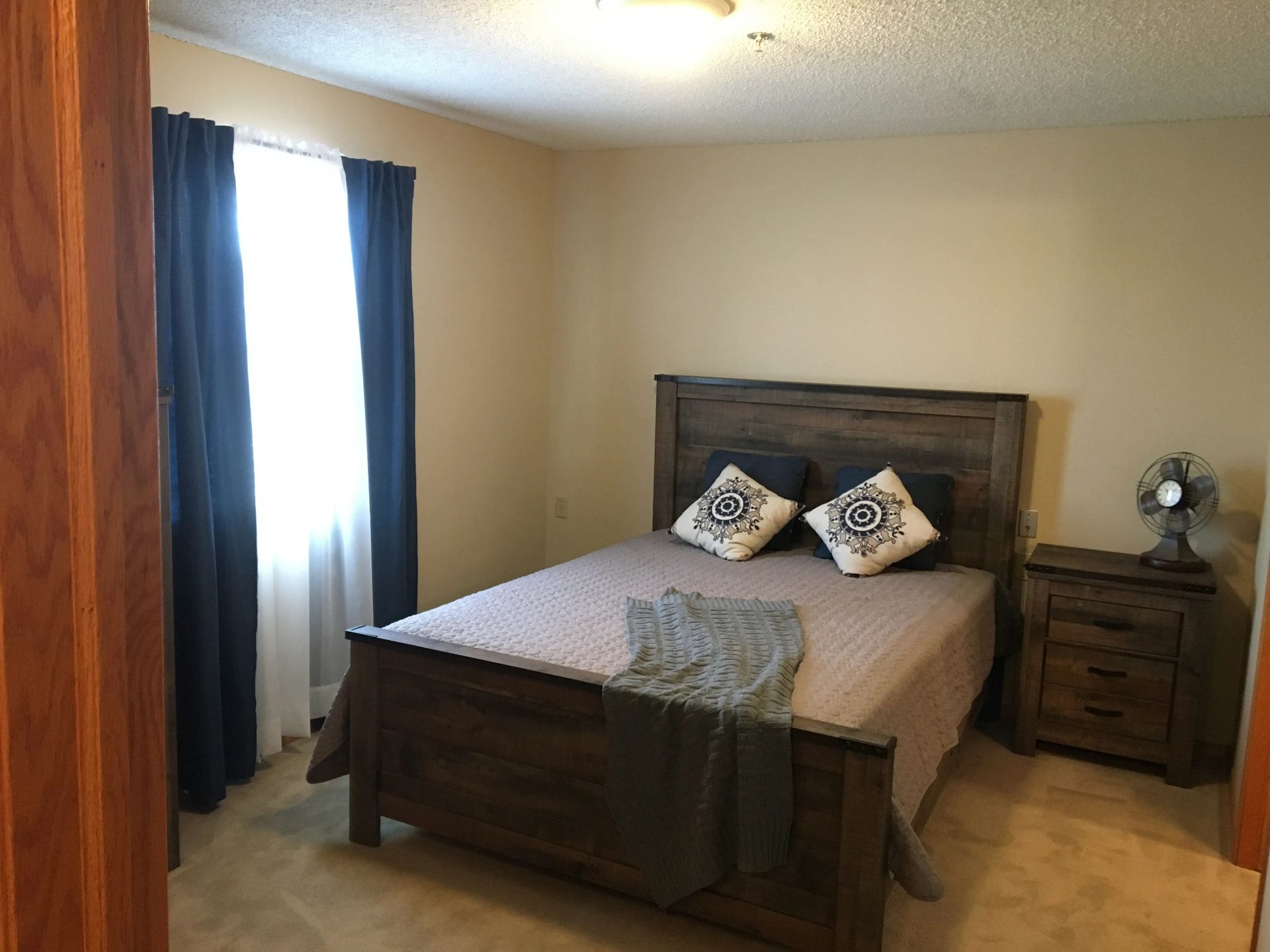 A bedroom with a bed, nightstand, and fan in an independent living facility.