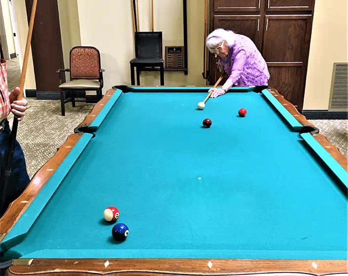 A woman is playing pool on a pool table in a retirement home.