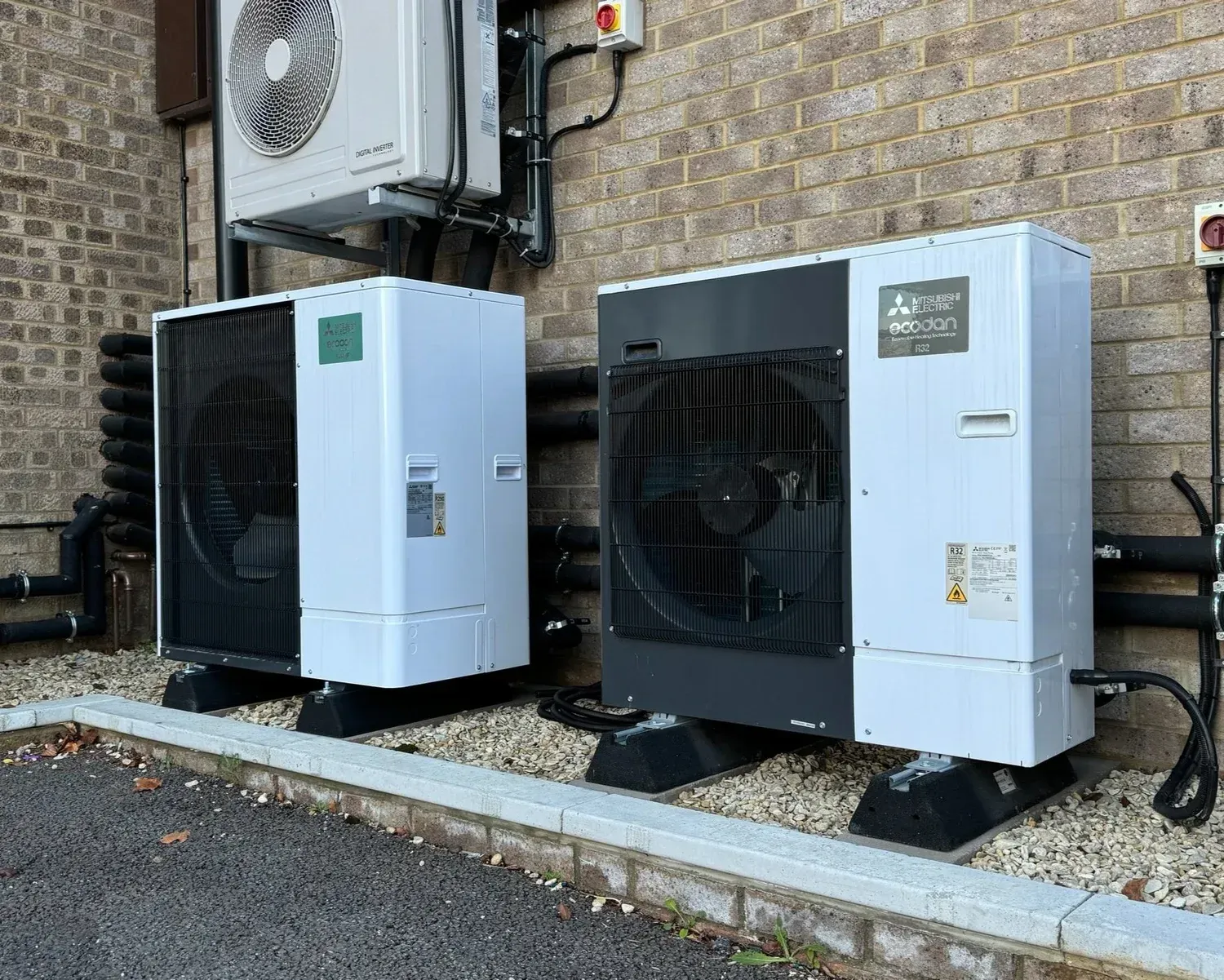 Two large outdoor HVAC units beside a brick building on gravel