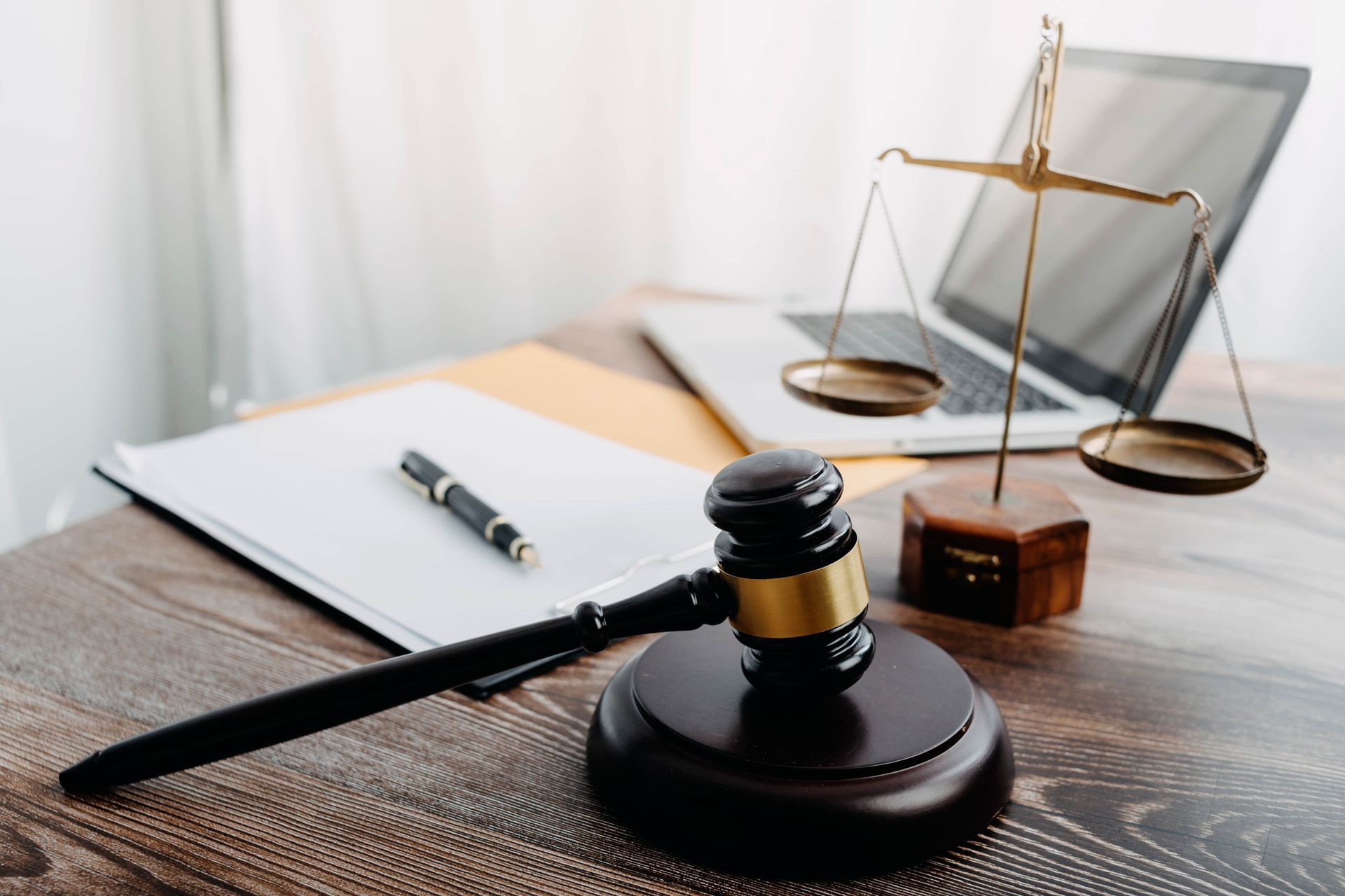 A judge's gavel is sitting on a wooden table next to a laptop and scales of justice.