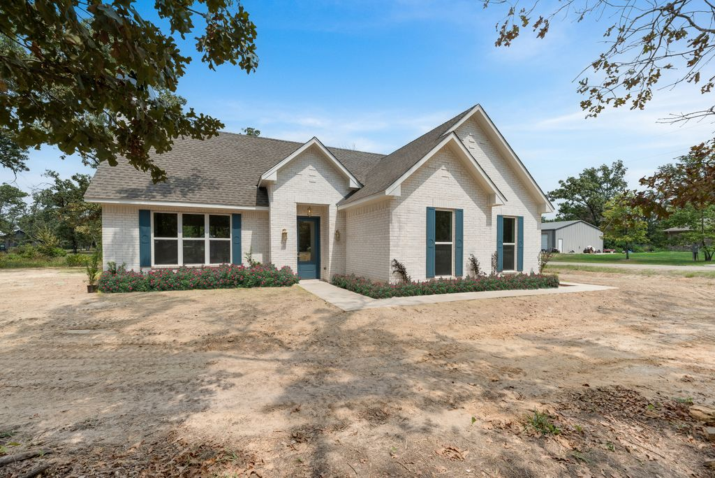 A light-colored brick house with blue shutters, a blue door, and a yard under construction.